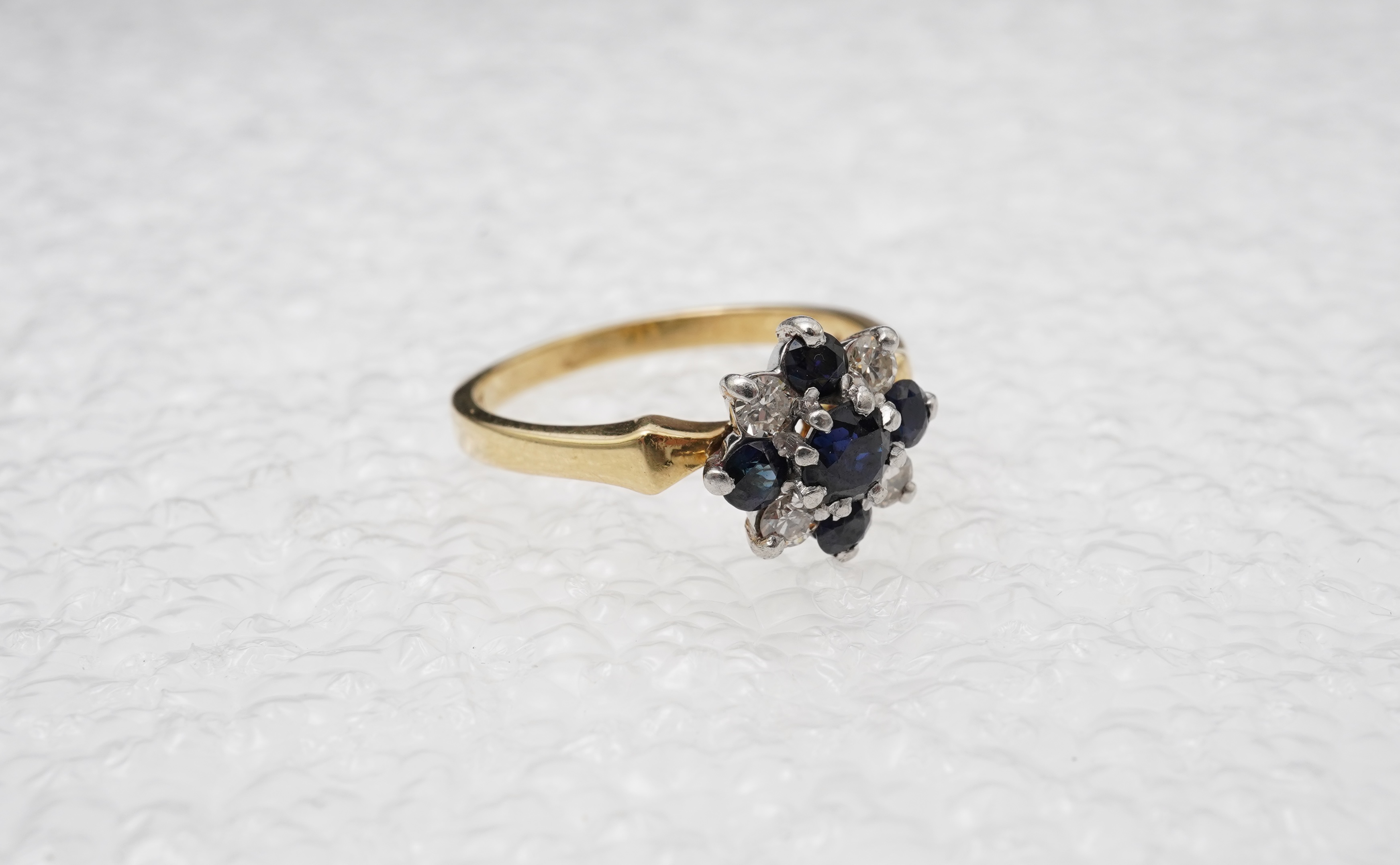 A sapphire and diamond cluster ring, set with circular-cut sapphires and brilliant-cut diamonds totalling approximately 0.20 carats, mounted in gold and platinum, size M, stamped 18CT PLAT, gross weight approximately 3.5